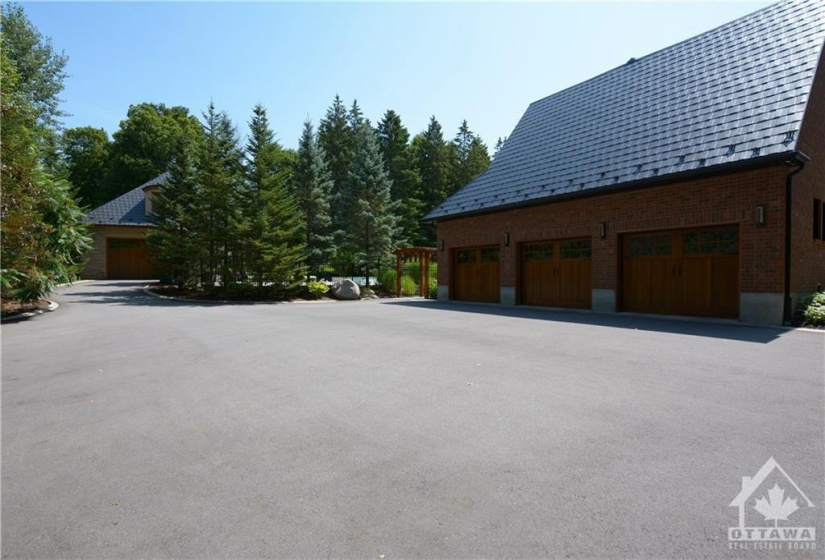 A great view of the steel roofing and the three car garage with wooden automatic doors. The paved driveway will easily accommodate parking for many guests. Enter to the pool area and yard from the Arbour beside the garage. The Guest house is at the top of the photo and also has a garage door making it easy to access the storage area of the guest house and store your lawn tractor. The main door to the guest house is to the left of the garage door of the guest house.