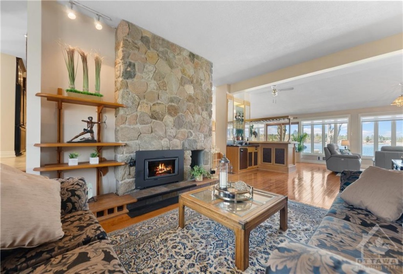 Beautiful living room with wood burning stone fireplace (insert).  Extra high ceilings in here and  the wet bar with mini fridge is in the distance for entertaining.  Gorgeous space.   Please note:  A fire has been virtually staged into the fireplace.