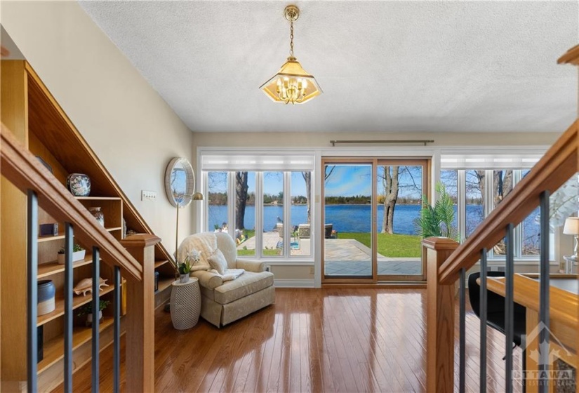 This stunning sunroom / entertainment space has wall to wall windows overlooking the river.  This is sunken from the kitchen.  Beautiful hardwood floors and artistic built in shelving unit are on both ends of this room.  Patio door to go to the water.  Look at this view!  Imagine sitting there looking out over the river... it is so peaceful.