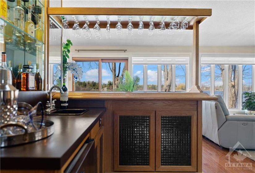 Beautiful wet bar with tons of storage on both sides of the bar, a bar fridge, glass shelving and it is a wetbar with a built in ice bucket on the top of the counter.