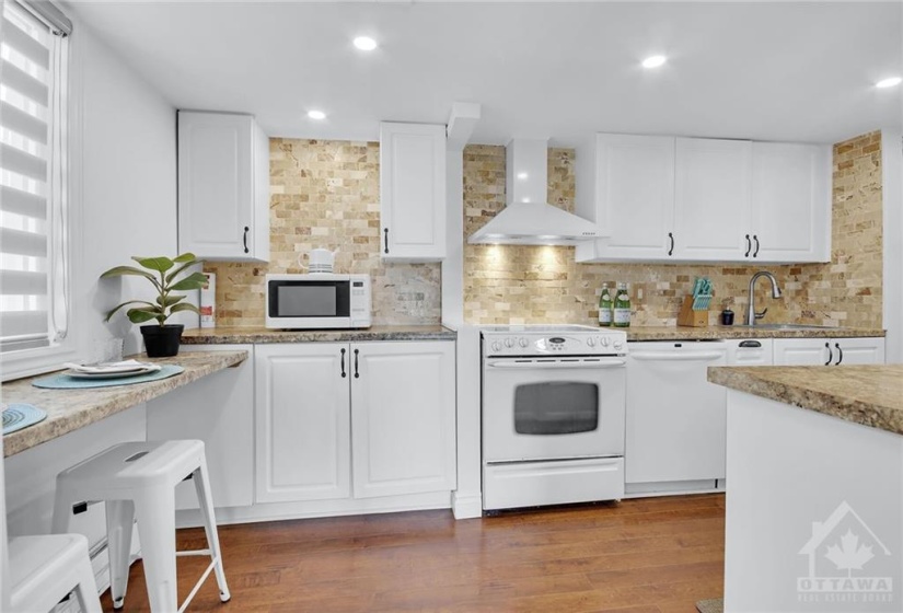 The bright white kitchen offers generous counter and cupboard space, a beautiful backsplash, pot lights, and a breakfast bar, perfect for morning meals